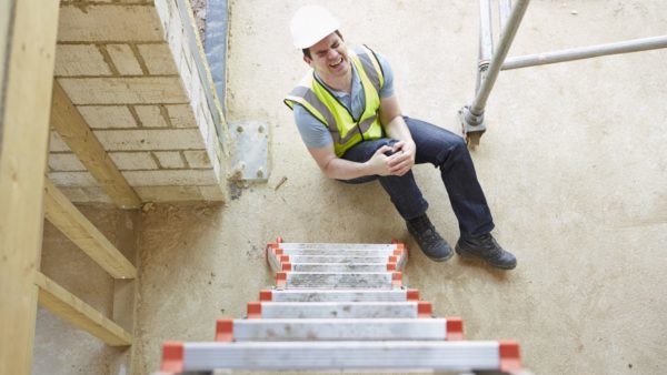 A man in a hi-vis jacket and hard hat holding his leg in pain after falling from a ladder (Image: Dreamstime)
